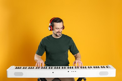 Photo of Smiling man in headphones playing synthesizer on orange background