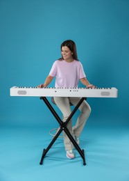 Photo of Smiling woman playing synthesizer on light blue background