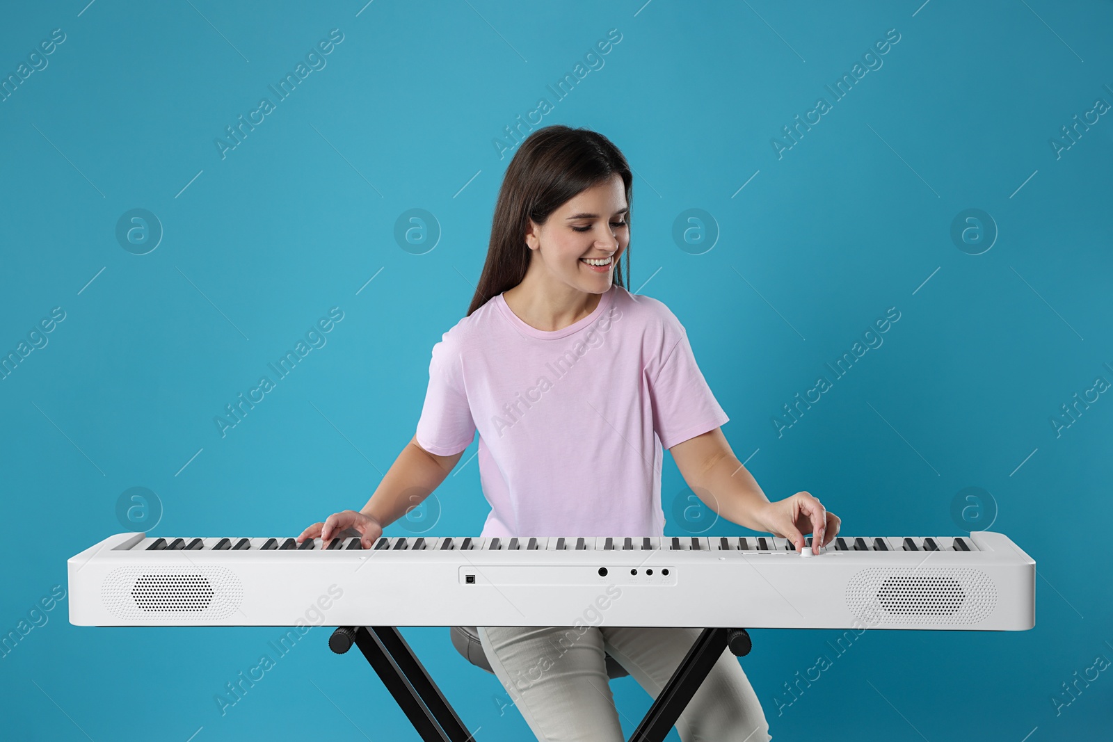 Photo of Smiling woman playing synthesizer on light blue background