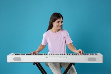 Photo of Smiling woman playing synthesizer on light blue background