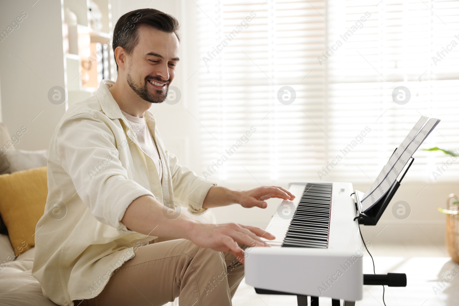 Photo of Smiling man playing synthesizer at home. Electronic musical instrument