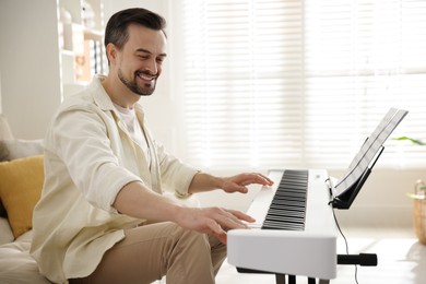 Photo of Smiling man playing synthesizer at home. Electronic musical instrument