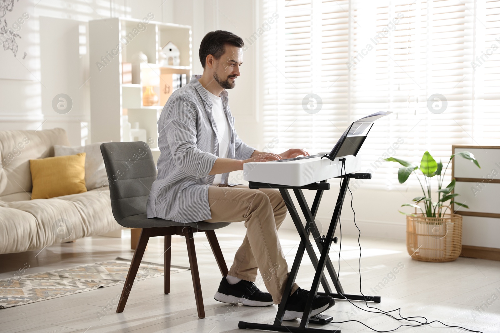 Photo of Bearded man playing synthesizer at home. Electronic musical instrument