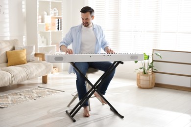 Photo of Smiling man playing synthesizer at home. Electronic musical instrument