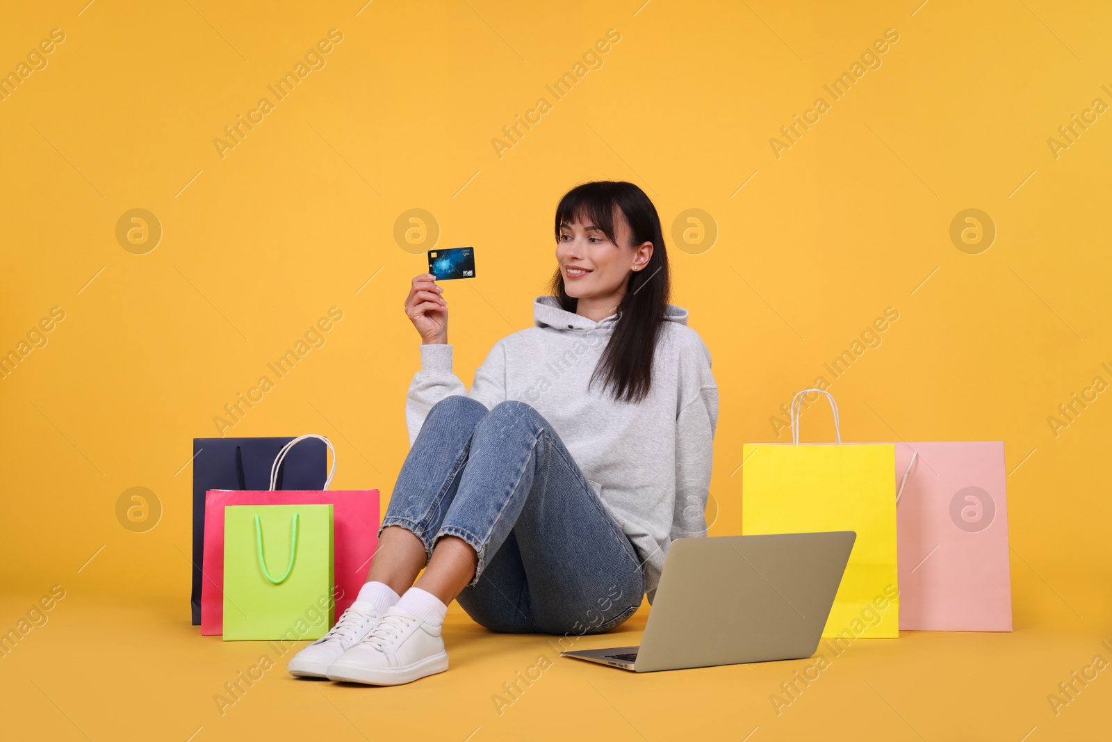 Photo of Internet shopping. Happy woman with credit card, laptop and colorful bags on orange background