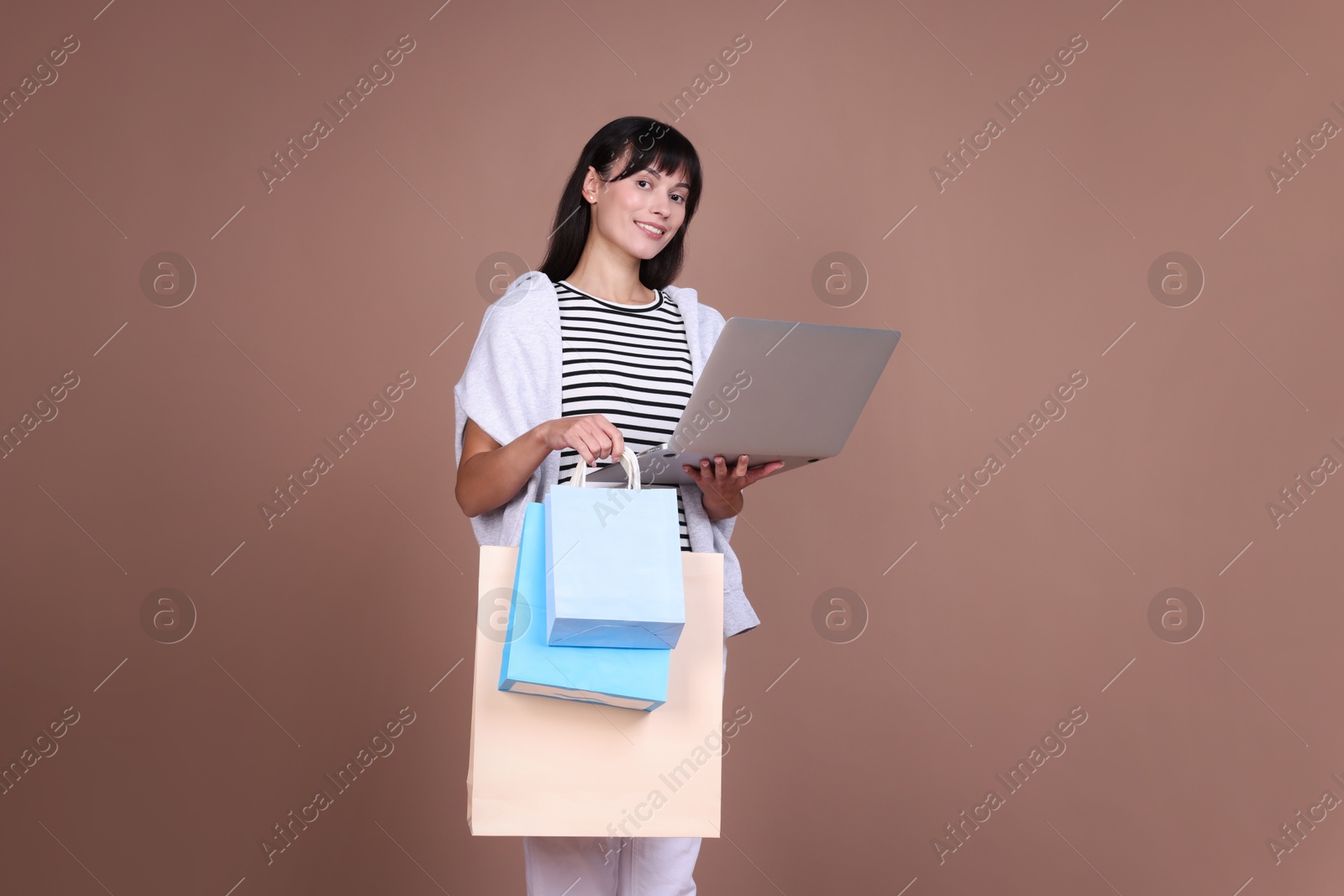 Photo of Internet shopping. Happy woman with laptop and colorful bags on beige background