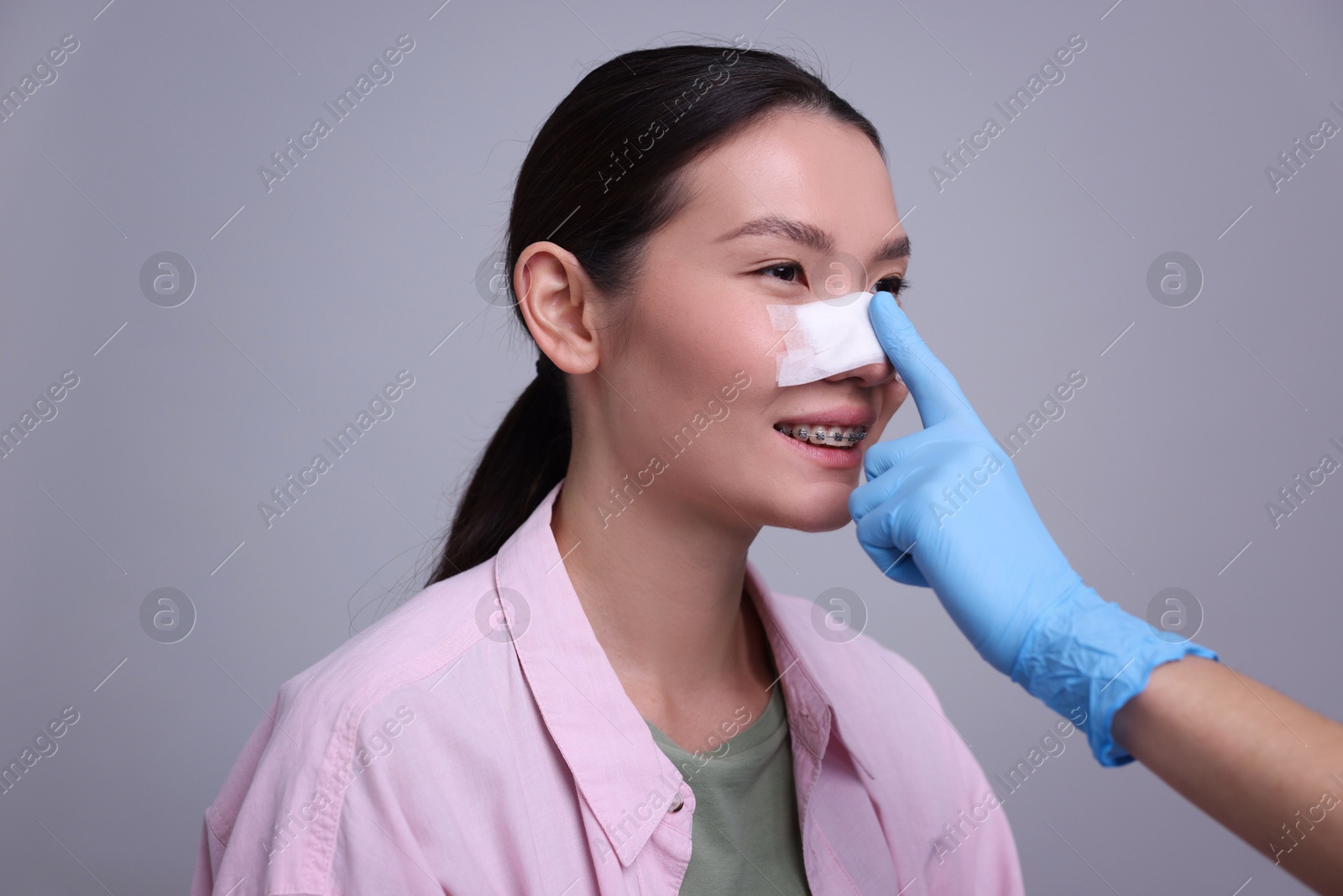 Photo of Doctor checking patient's nose after plastic surgery operation on light grey background, closeup