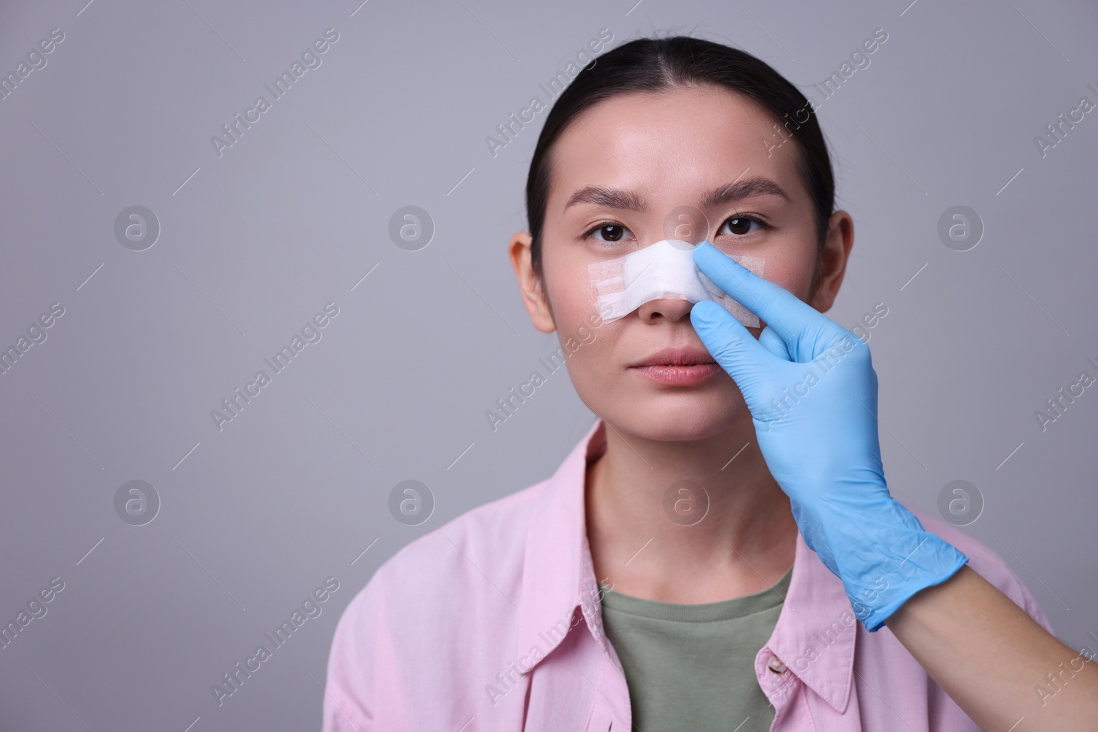 Photo of Doctor checking patient's nose after plastic surgery operation on light grey background, closeup. Space for text