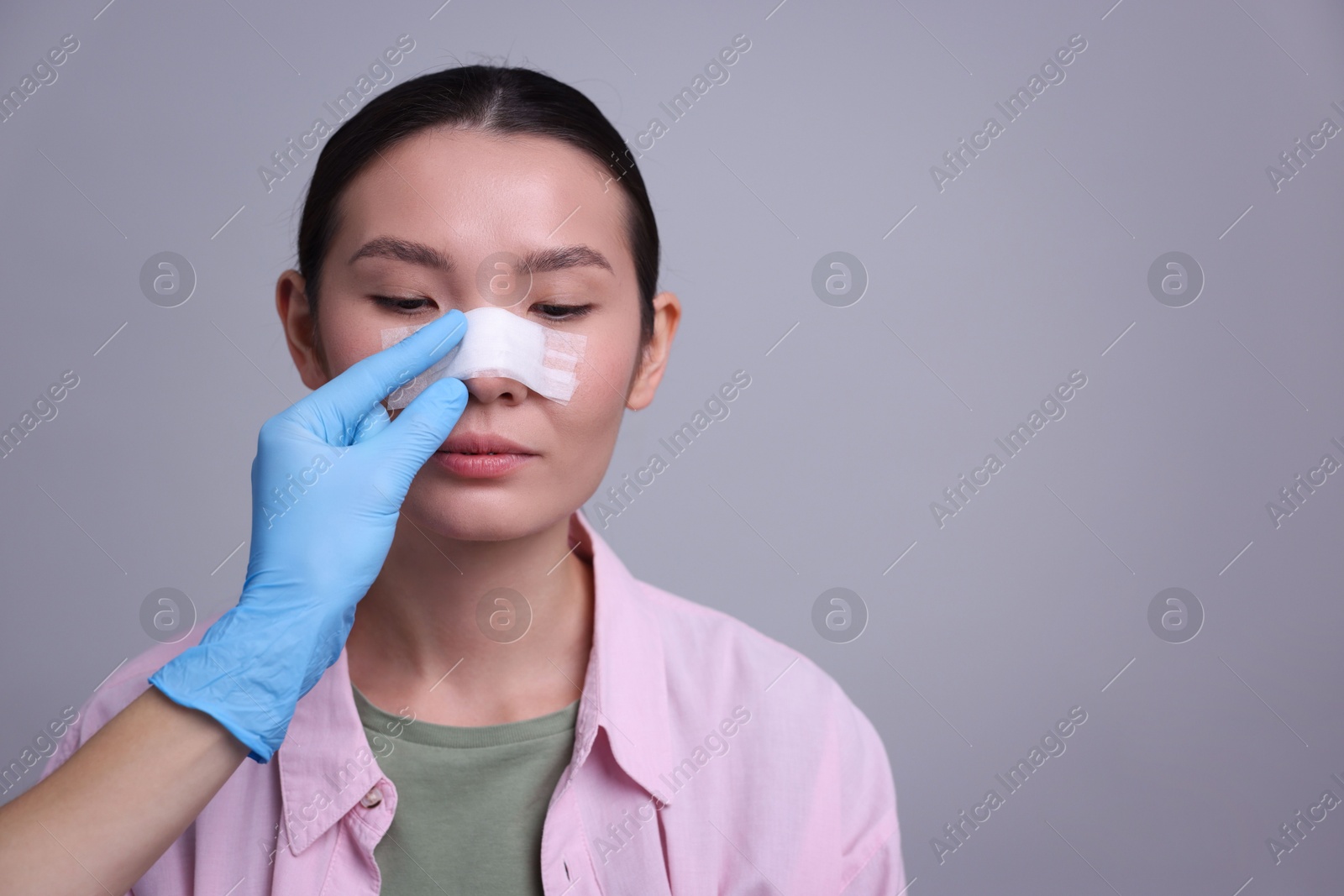 Photo of Doctor checking patient's nose after plastic surgery operation on light grey background, closeup. Space for text