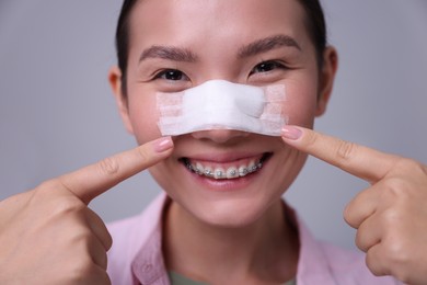 Photo of Woman with medical bandage on her nose after plastic surgery operation against light grey background, closeup