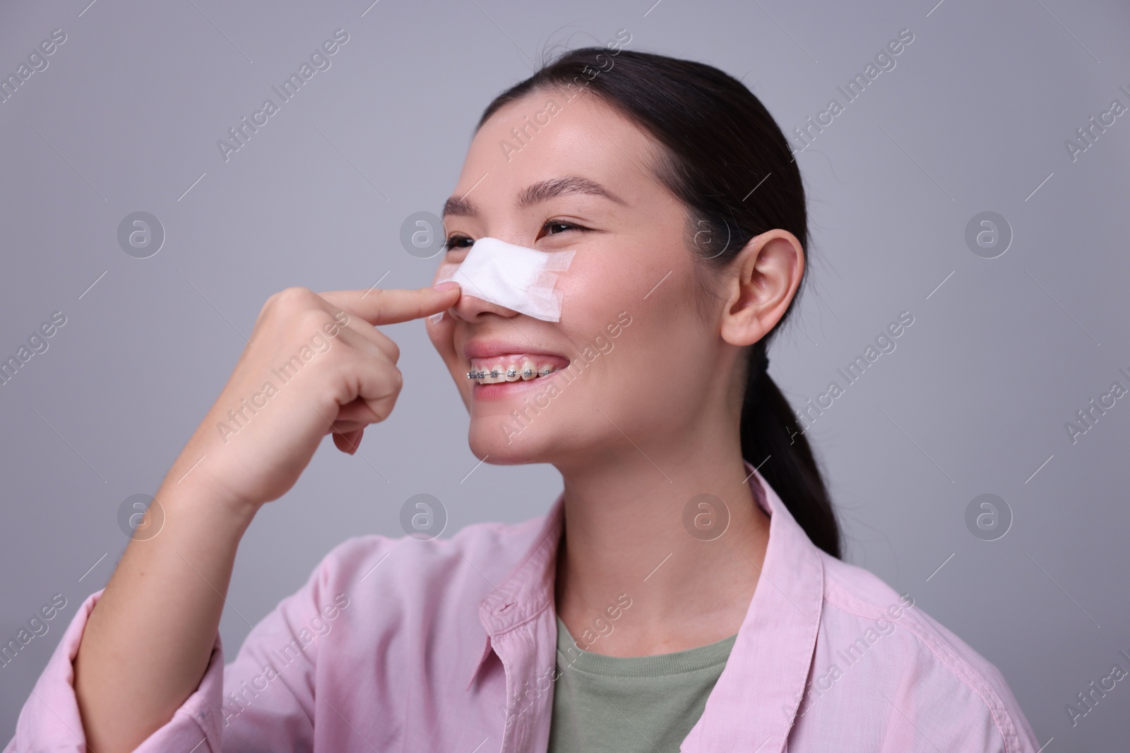 Photo of Woman with medical bandage on her nose after plastic surgery operation against light grey background