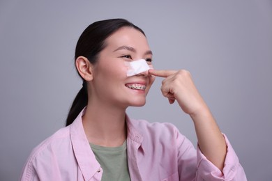 Photo of Woman with medical bandage on her nose after plastic surgery operation against light grey background