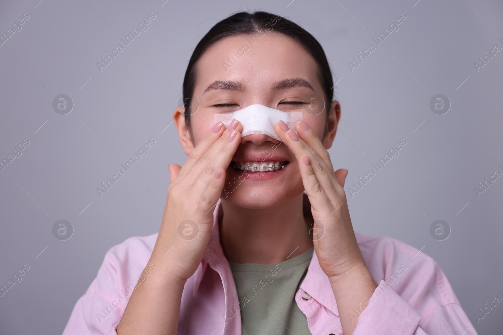 Photo of Woman with medical bandage on her nose after plastic surgery operation against light grey background