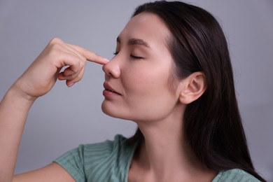 Photo of Woman touching her nose on light grey background, closeup