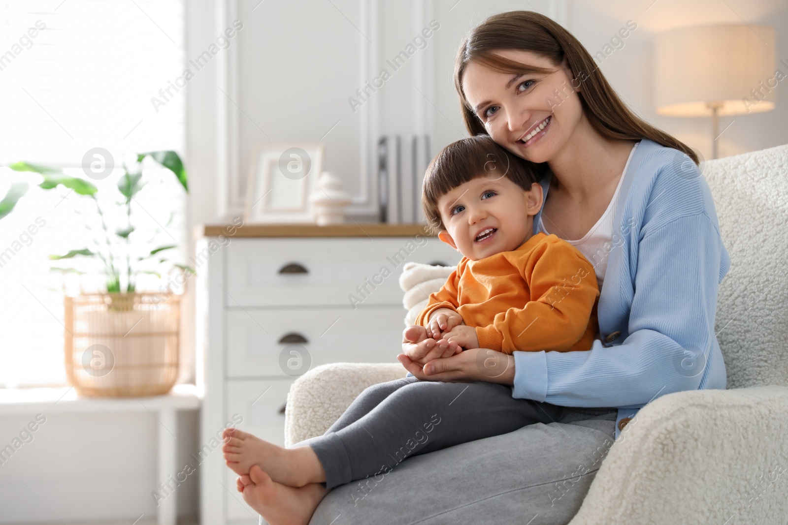 Photo of Happy mother with her little son sitting on armchair at home. Space for text