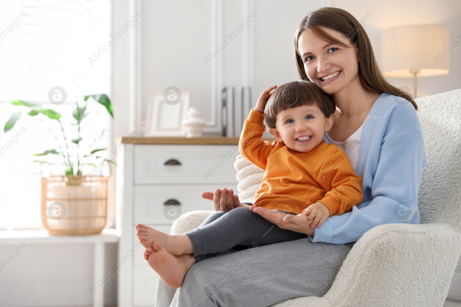 Photo of Happy mother with her little son sitting on armchair at home. Space for text