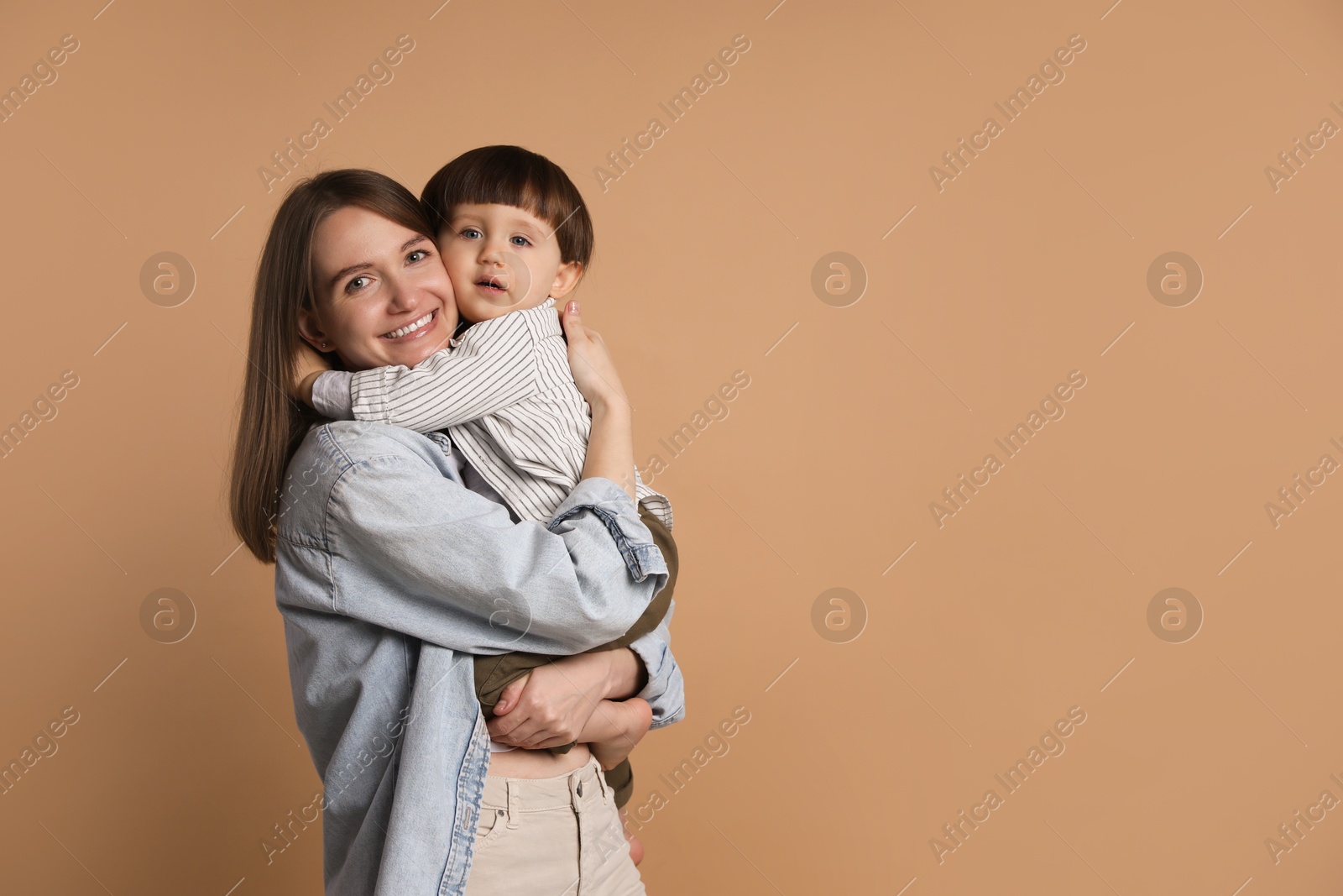 Photo of Family portrait of happy mother hugging her little son on beige background. Space for text