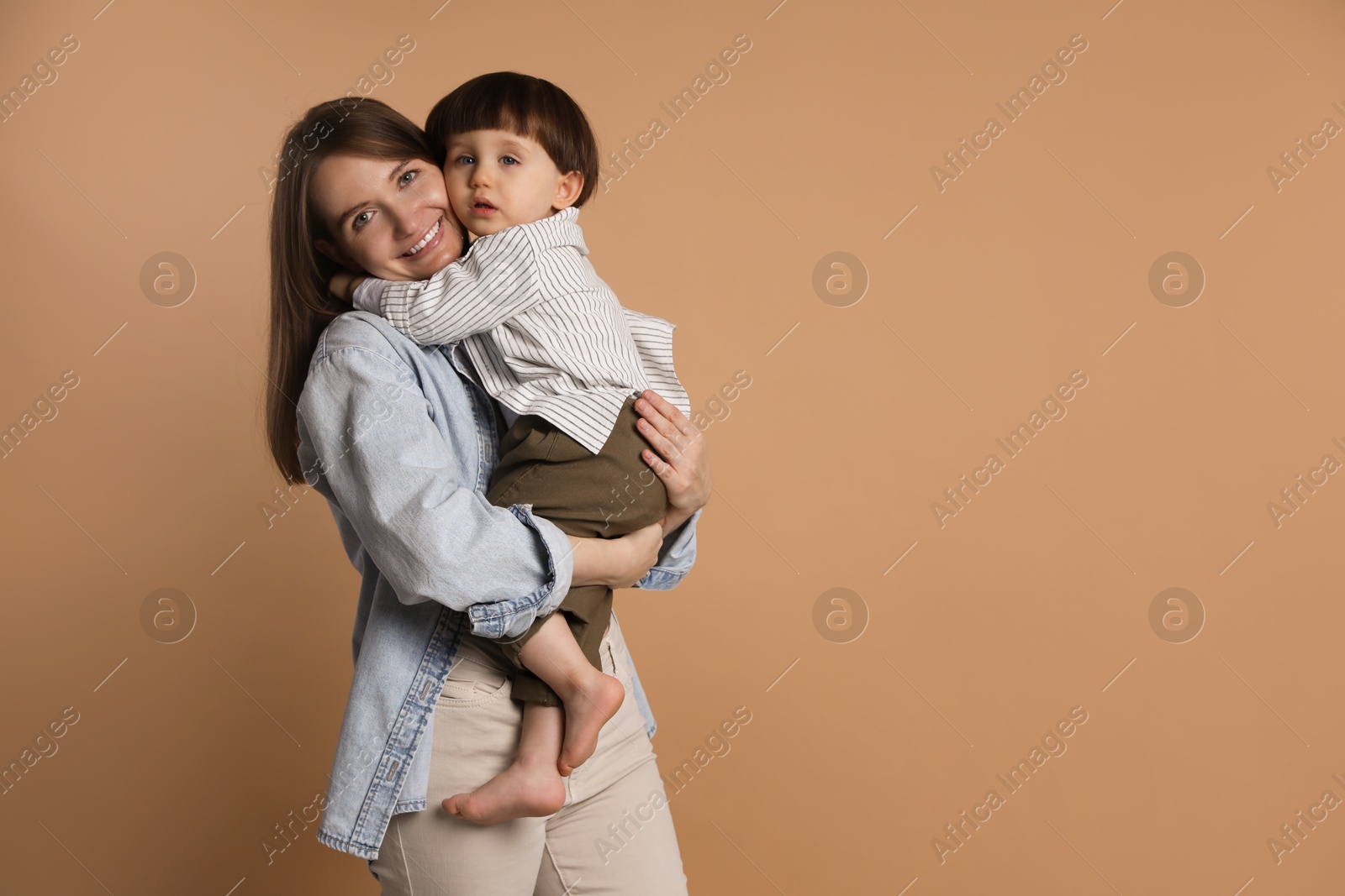 Photo of Family portrait of happy mother hugging her little son on beige background. Space for text