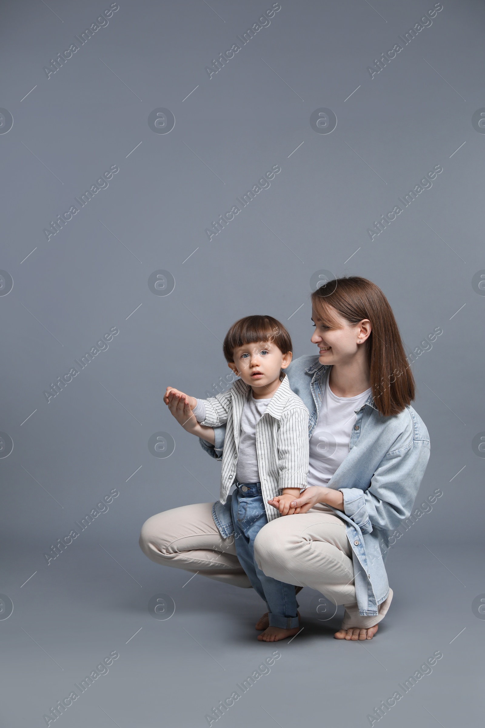 Photo of Happy mother with her little son on grey background. Space for text