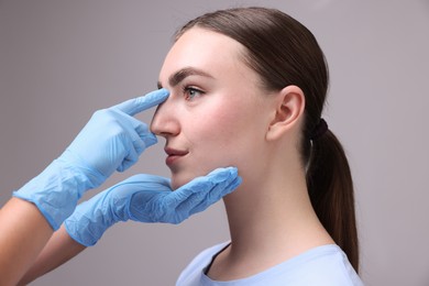 Photo of Doctor checking patient's nose before plastic surgery operation on grey background, closeup