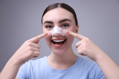 Photo of Woman with medical bandage on her nose after plastic surgery operation against grey background