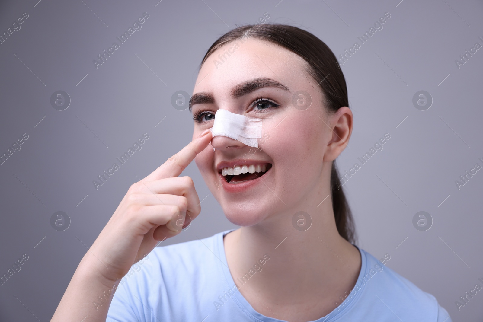 Photo of Woman with medical bandage on her nose after plastic surgery operation against grey background