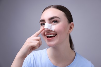 Photo of Woman with medical bandage on her nose after plastic surgery operation against grey background