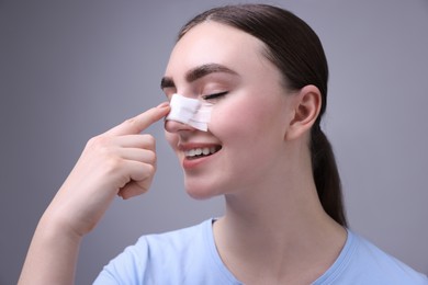 Photo of Woman with medical bandage on her nose after plastic surgery operation against grey background