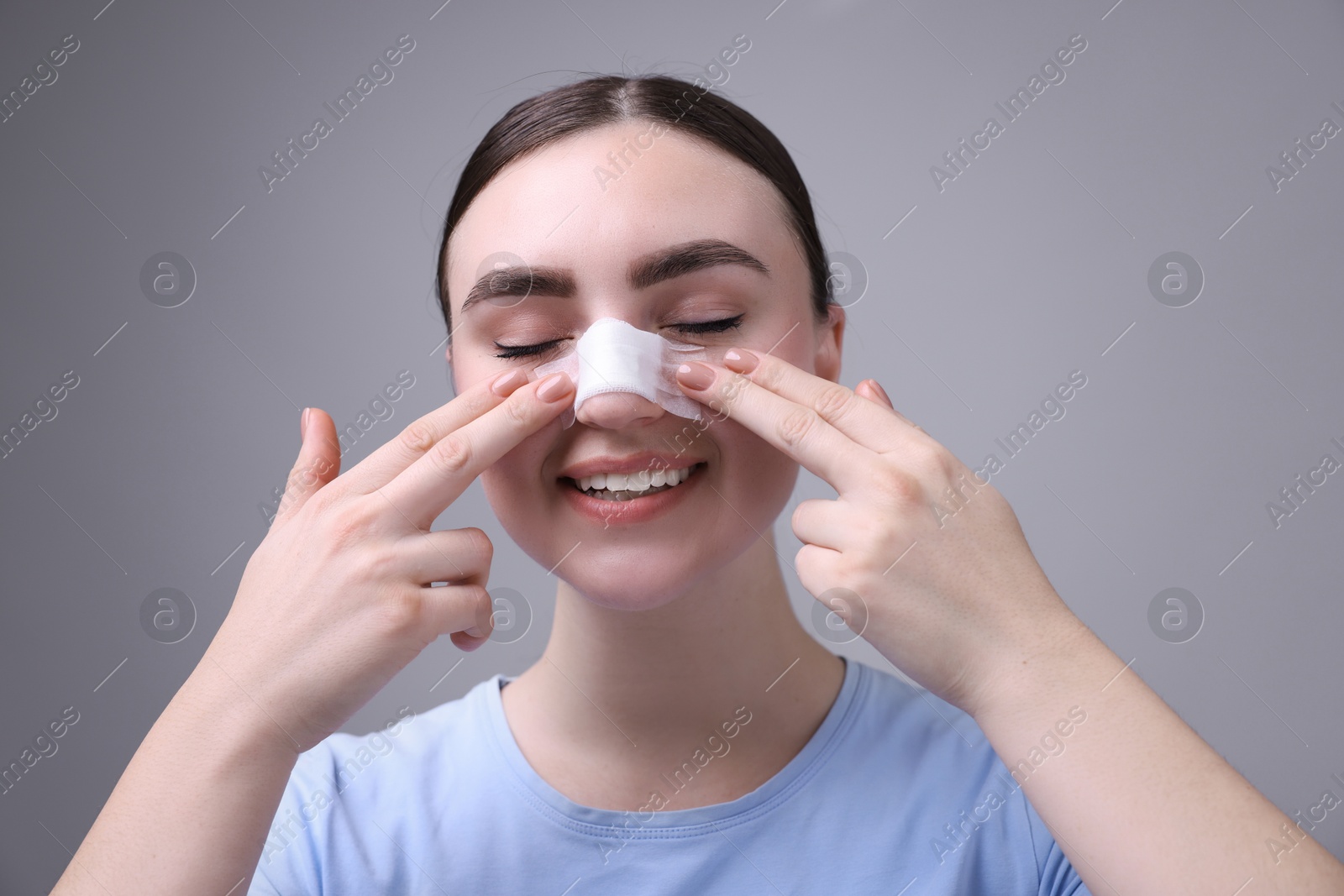 Photo of Woman with medical bandage on her nose after plastic surgery operation against grey background