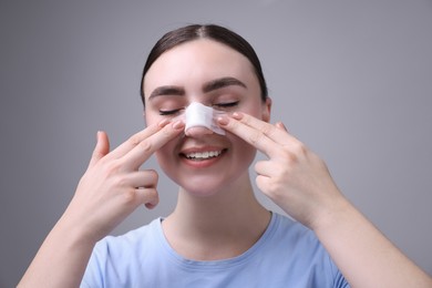 Photo of Woman with medical bandage on her nose after plastic surgery operation against grey background