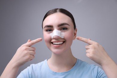 Photo of Woman with medical bandage on her nose after plastic surgery operation against grey background