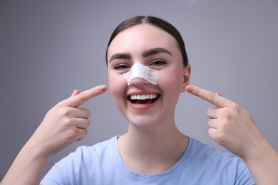 Photo of Woman with medical bandage on her nose after plastic surgery operation against grey background