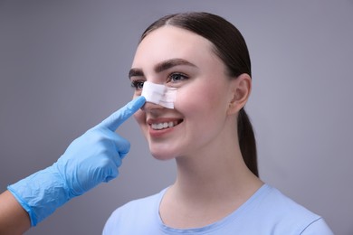 Photo of Doctor checking patient's nose after plastic surgery operation on grey background, closeup