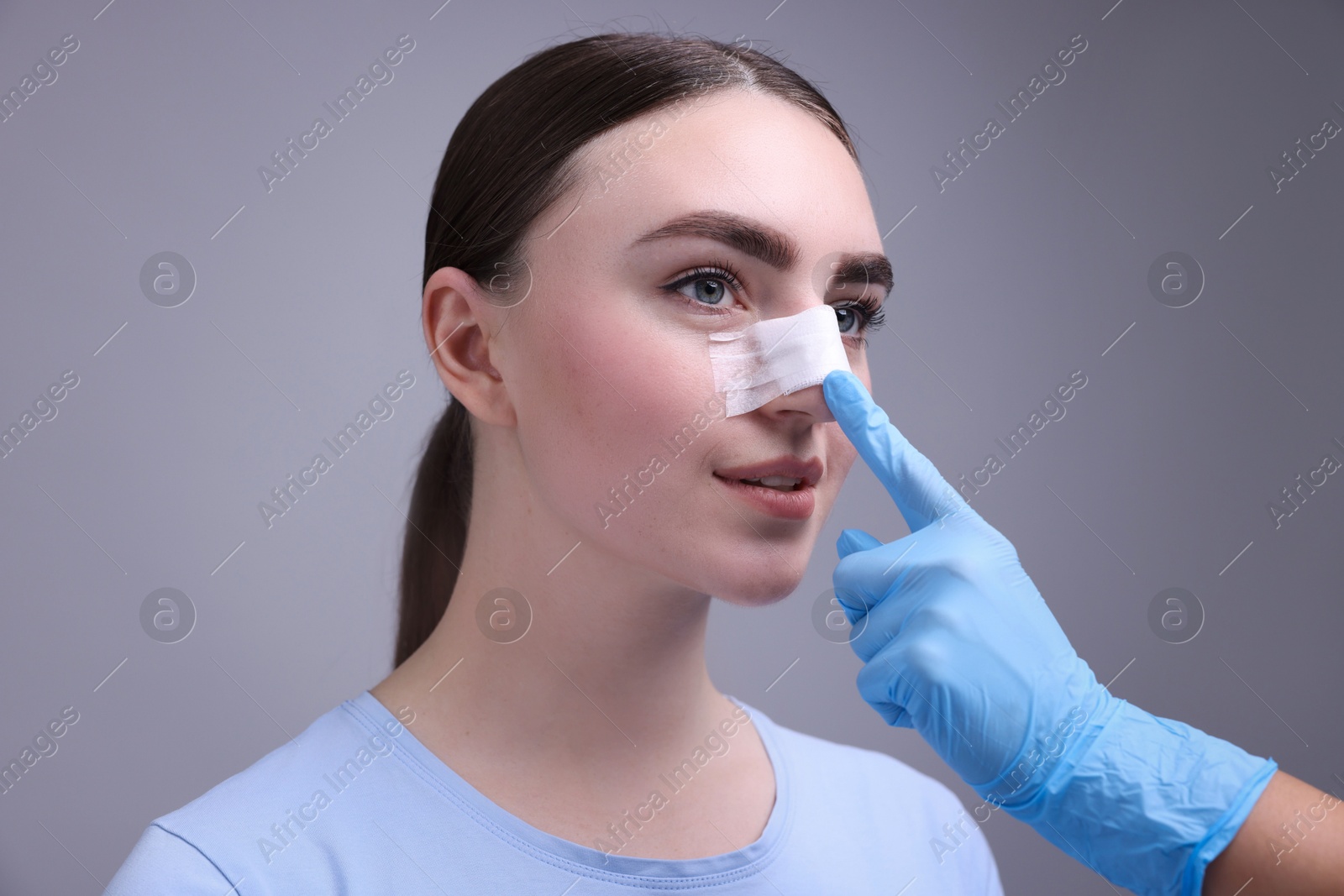 Photo of Doctor checking patient's nose after plastic surgery operation on grey background, closeup