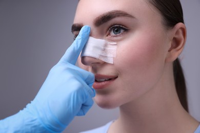 Photo of Doctor checking patient's nose after plastic surgery operation on grey background, closeup