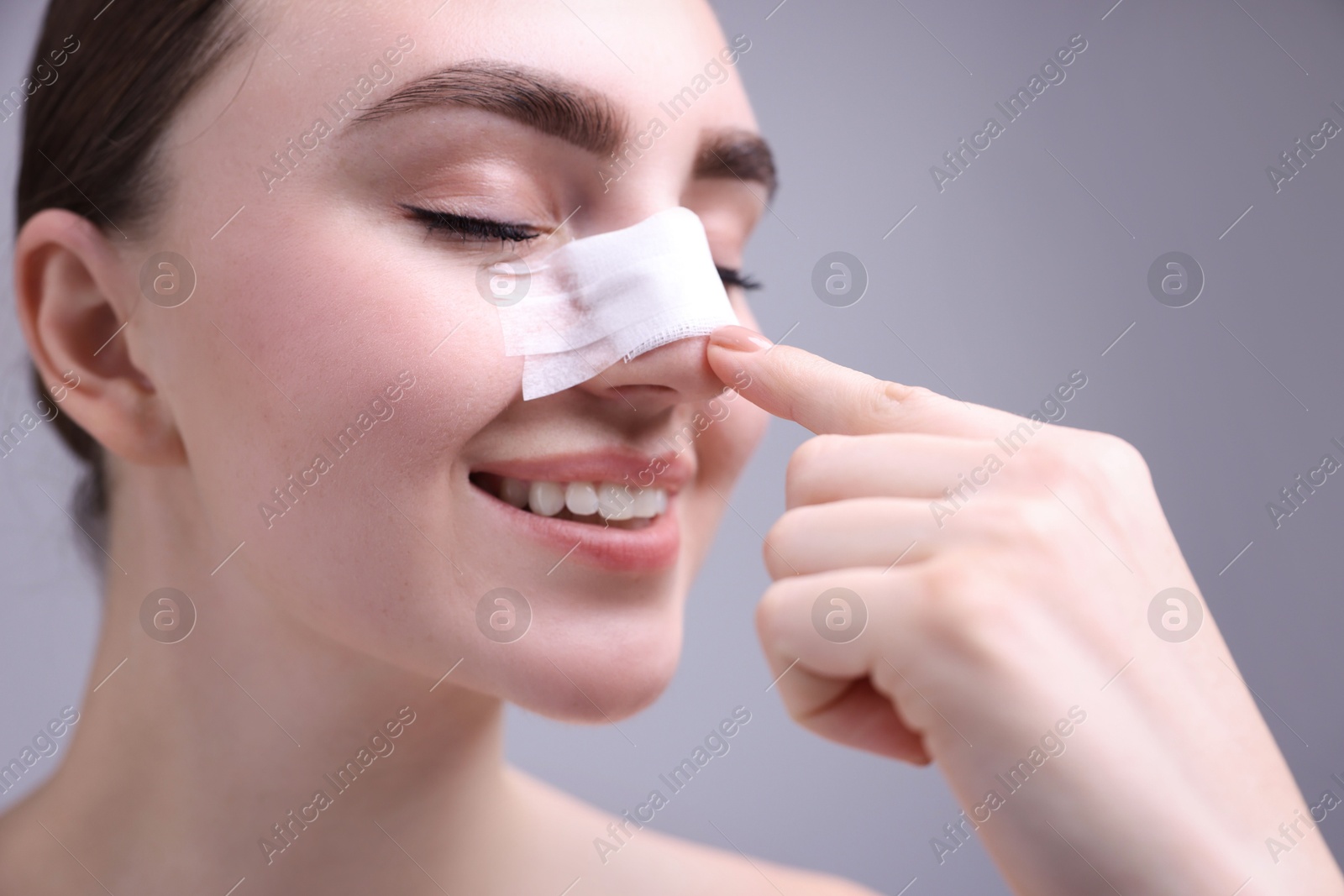 Photo of Woman with medical bandage on her nose after plastic surgery operation against grey background