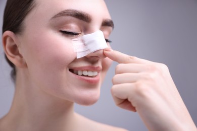 Woman with medical bandage on her nose after plastic surgery operation against grey background