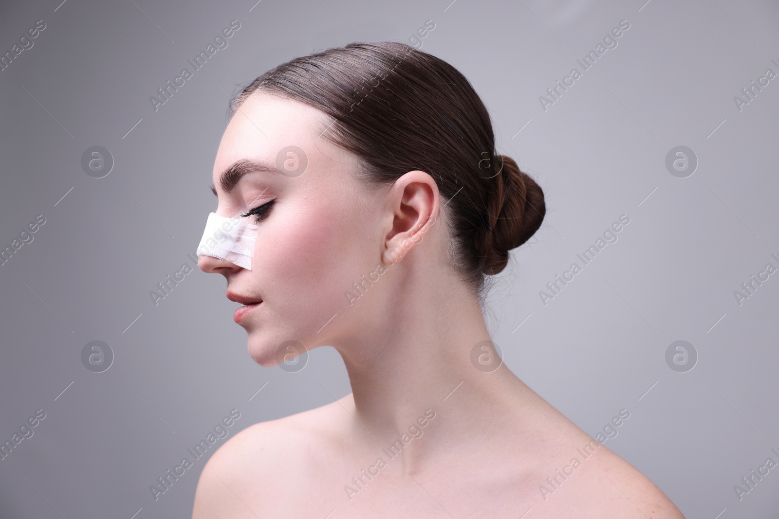 Photo of Woman with medical bandage on her nose after plastic surgery operation against grey background