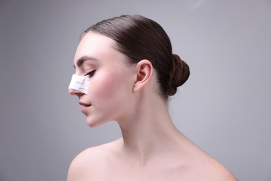 Photo of Woman with medical bandage on her nose after plastic surgery operation against grey background