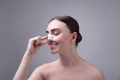 Photo of Woman with medical bandage on her nose after plastic surgery operation against grey background