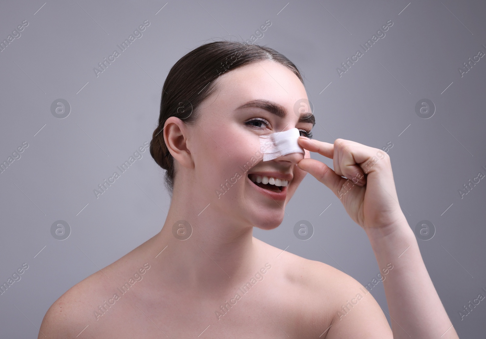 Photo of Woman with medical bandage on her nose after plastic surgery operation against grey background