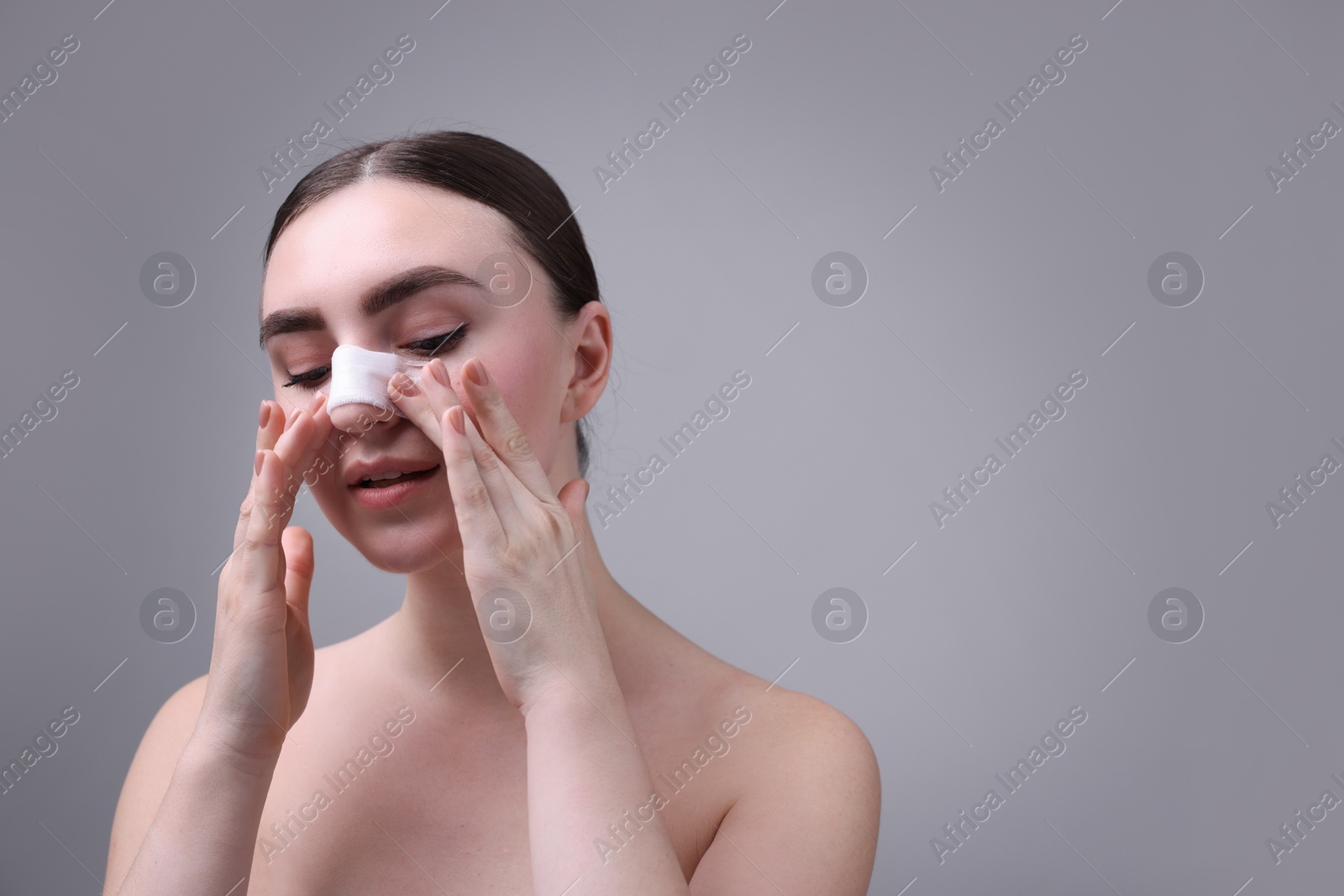 Photo of Woman with medical bandage on her nose after plastic surgery operation against grey background, space for text