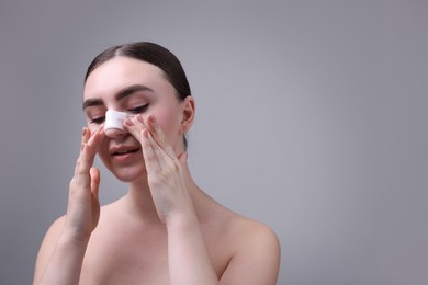 Photo of Woman with medical bandage on her nose after plastic surgery operation against grey background, space for text