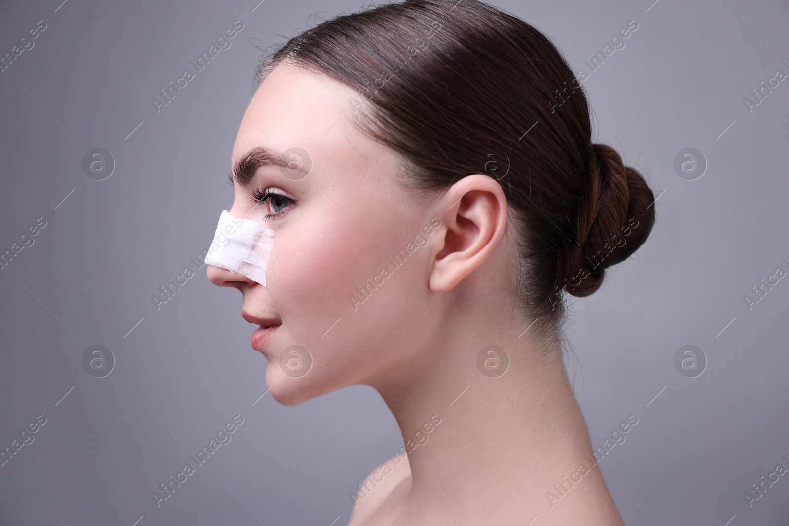 Photo of Woman with medical bandage on her nose after plastic surgery operation against grey background