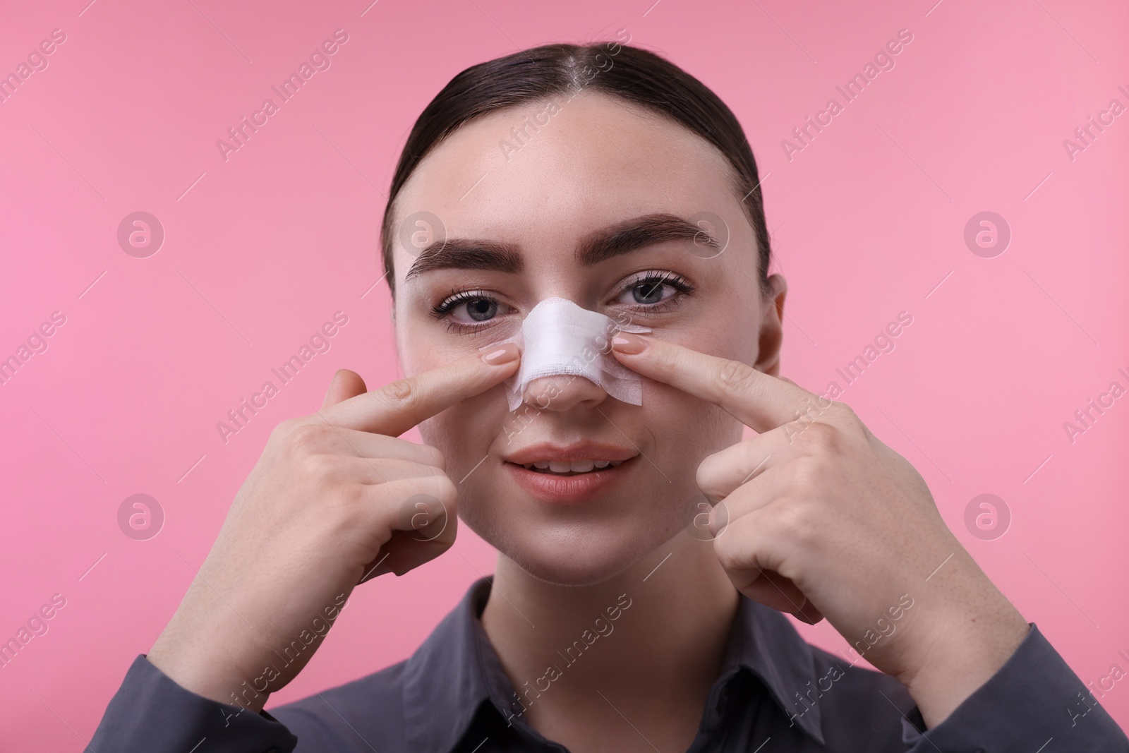 Photo of Woman with medical bandage on her nose after plastic surgery operation against pink background