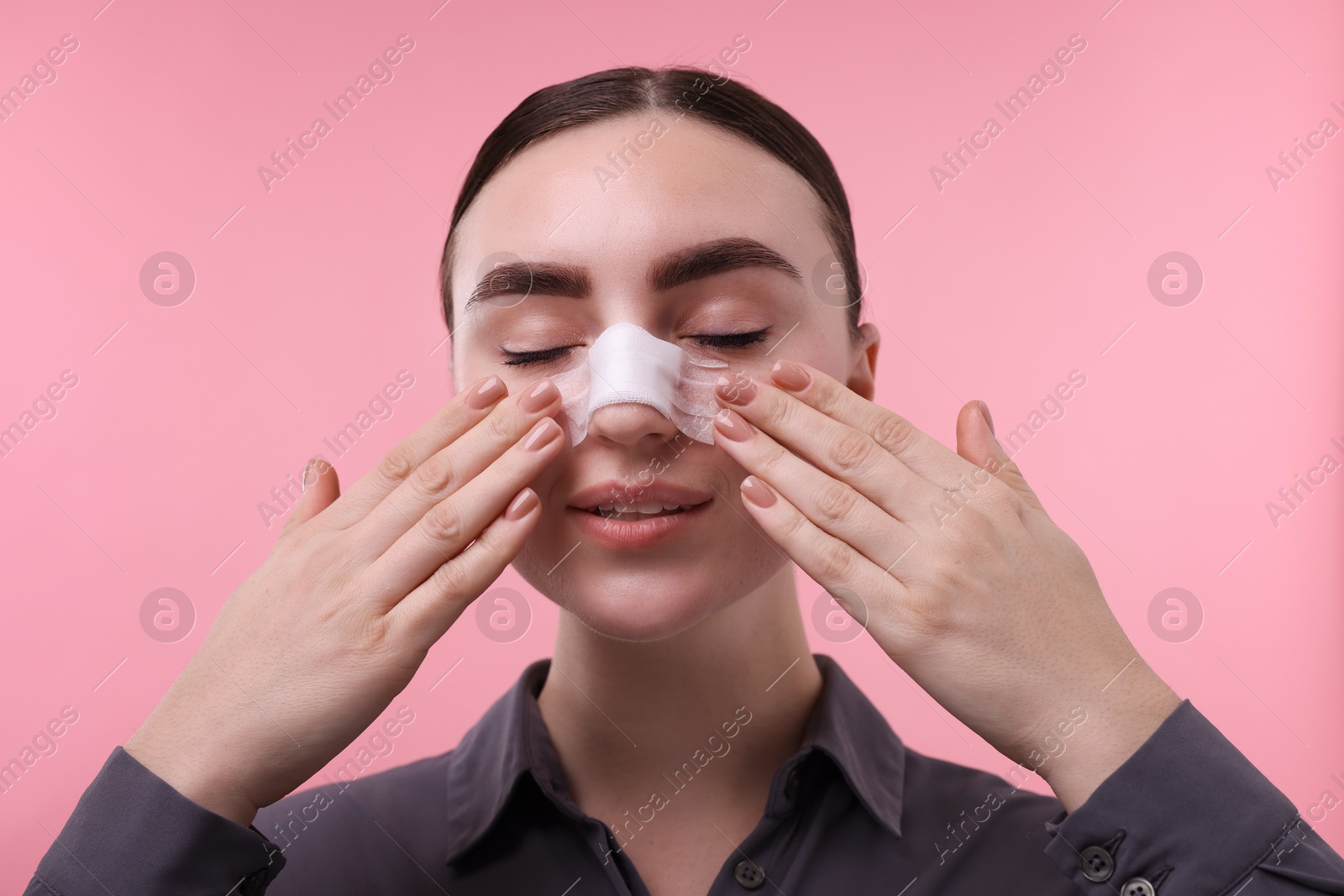 Photo of Woman with medical bandage on her nose after plastic surgery operation against pink background