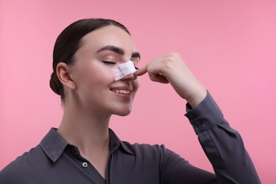 Woman with medical bandage on her nose after plastic surgery operation against pink background