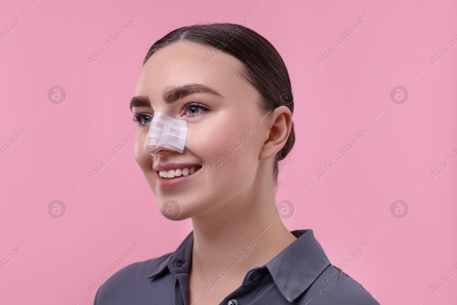 Photo of Woman with medical bandage on her nose after plastic surgery operation against pink background