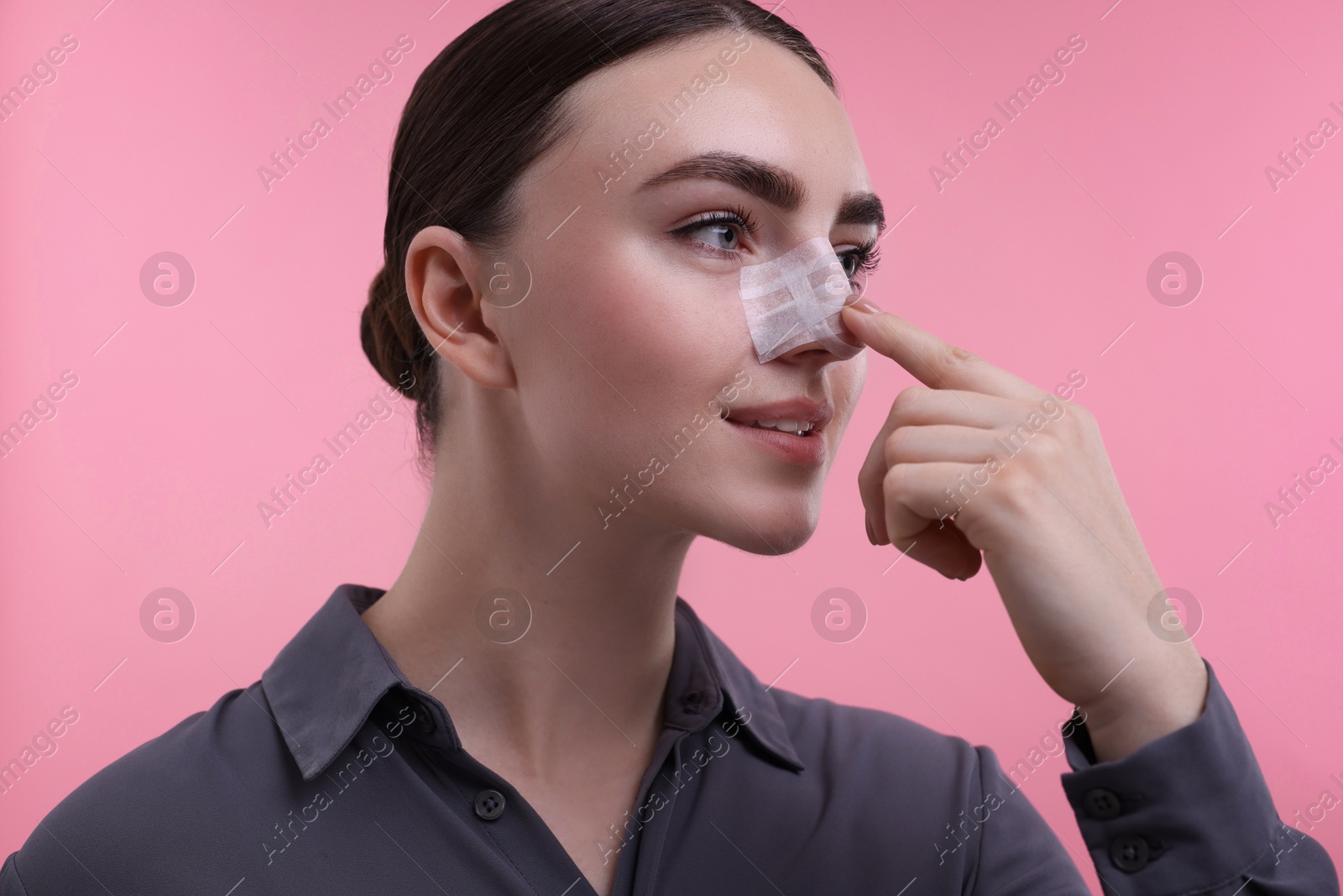 Photo of Woman with medical bandage on her nose after plastic surgery operation against pink background