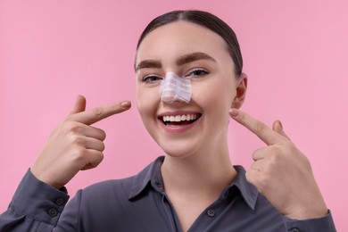 Photo of Woman with medical bandage on her nose after plastic surgery operation against pink background